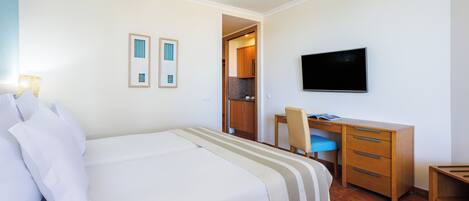 A hotel room with a bed, a desk, a chair, a television, and a door leading to a kitchenette.