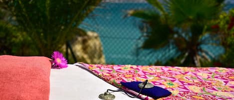 A bed with a colorful patterned bedspread, a red towel, and a decorative item on the side.