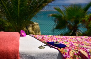 Una cama con una colcha estampada y colorida, una toalla roja y un objeto decorativo al lado.