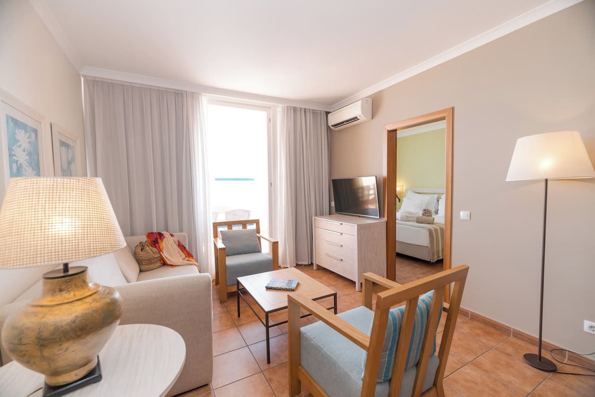 A hotel room with a sofa, armchair, dining table, TV, and a large mirror.