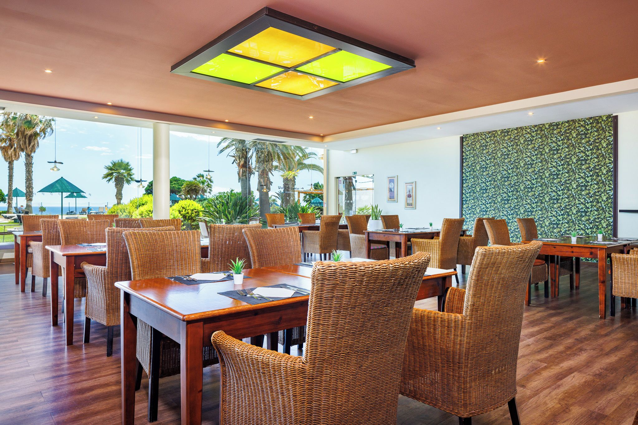 A restaurant with wicker furniture, large windows, and a view of palm trees.