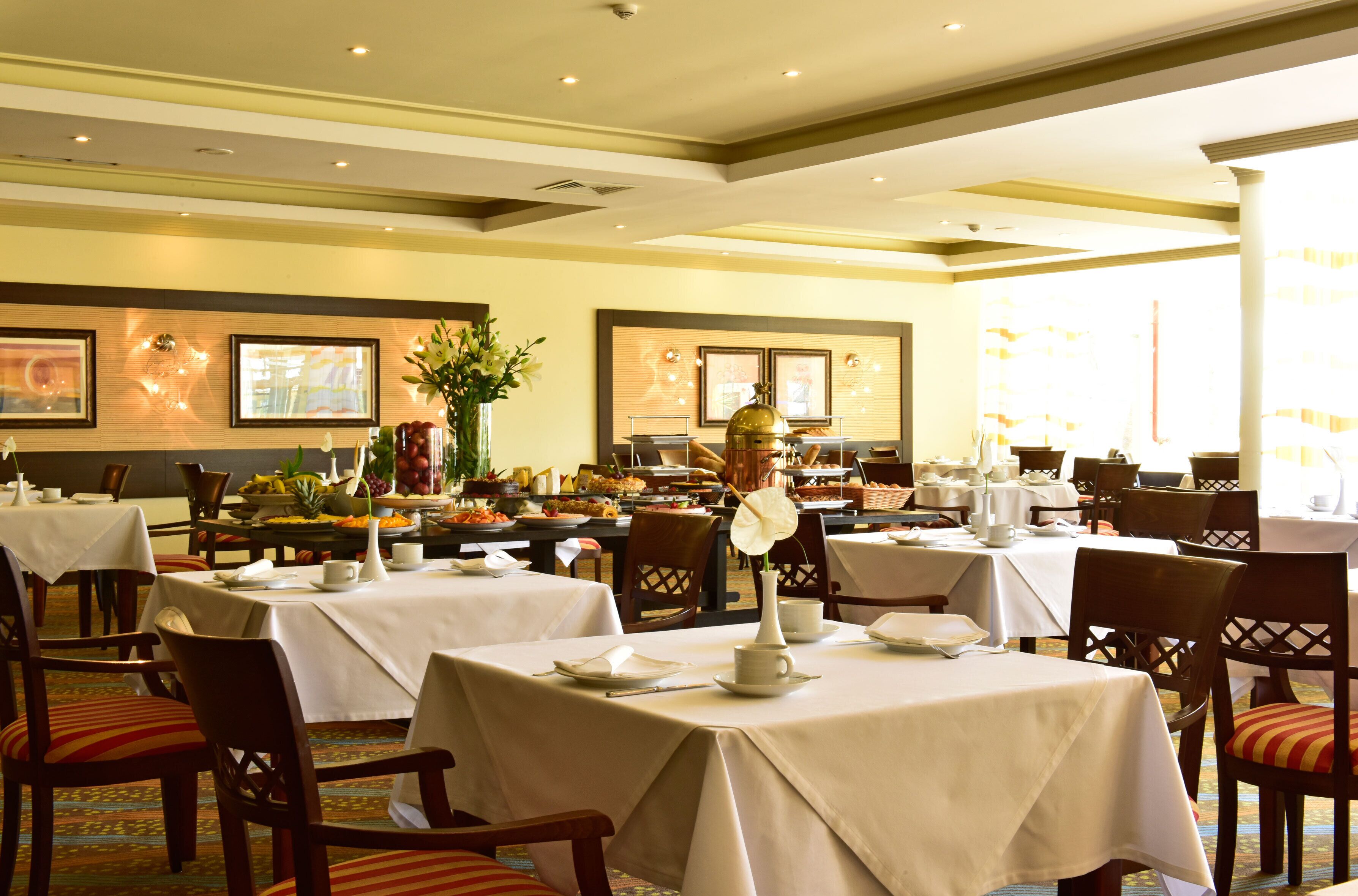 A dining area with tables set for breakfast, featuring a variety of food items and a decorative centerpiece.