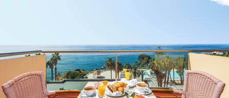 A balcony with a table set for breakfast overlooking a beach and ocean.