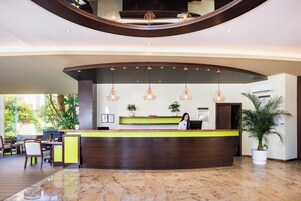 A reception desk with a person standing behind it, a computer, and a plant on the desk.