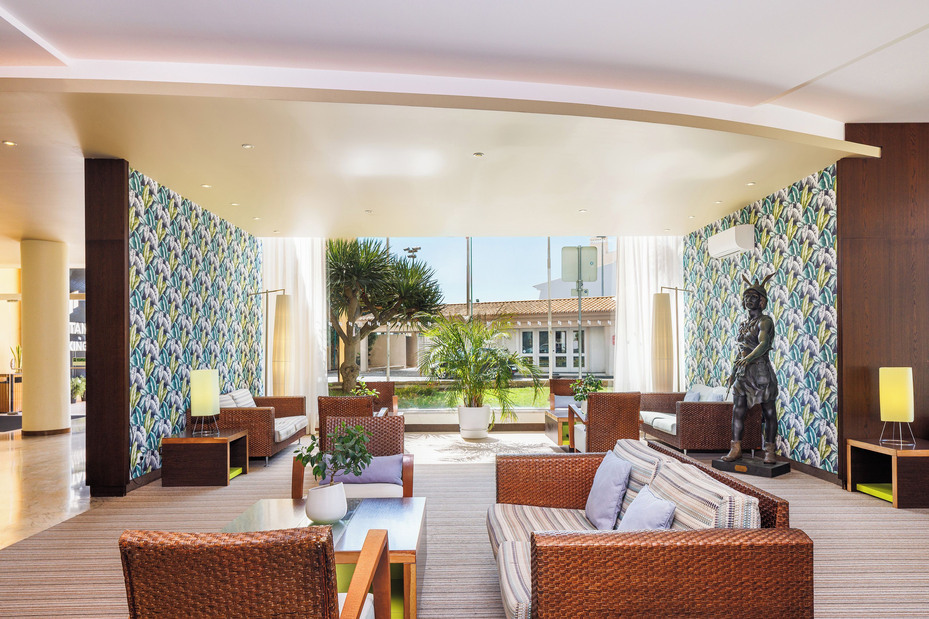 A spacious lobby with wicker furniture, a statue, and a view of the outside.