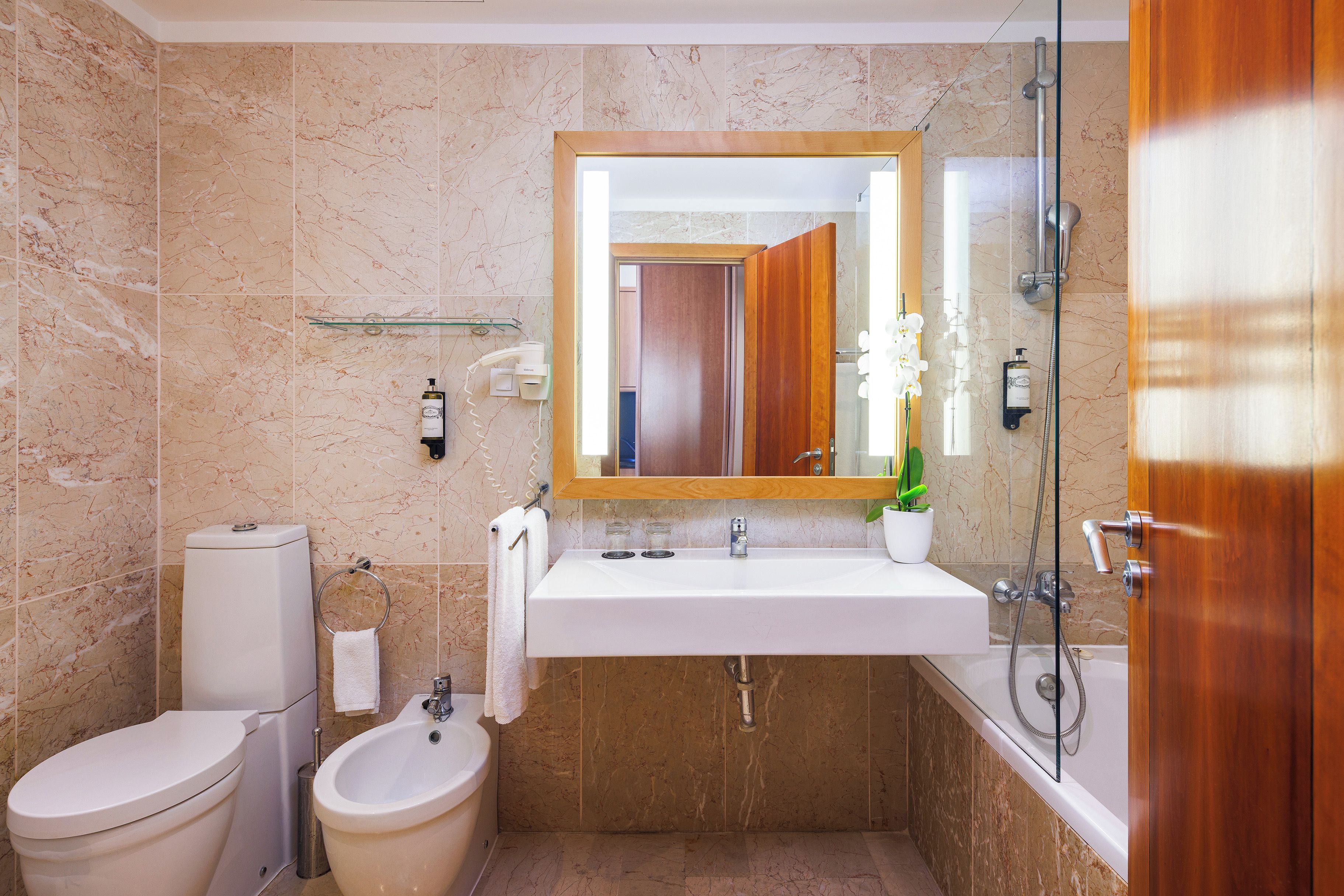 A bathroom with a marble wall, a white sink, a bidet, a toilet, and a shower.