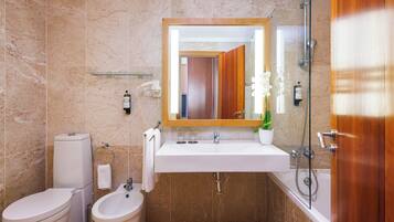 A bathroom with a marble wall, a white sink, a bidet, a toilet, and a shower.