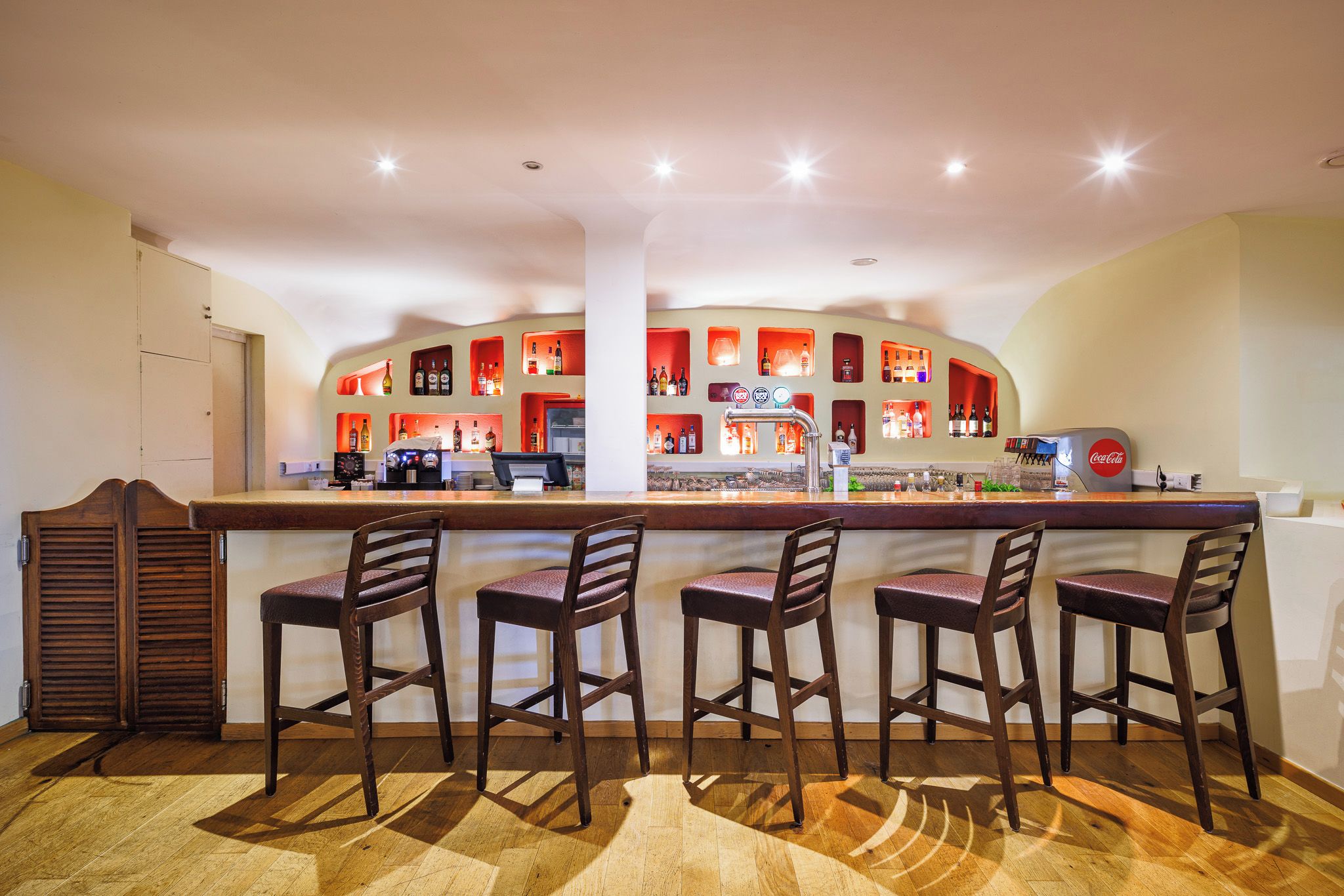 Una zona de bar con mostrador, taburetes y estanterías llenas de botellas.
