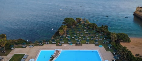 Un resort con una amplia piscina, sillas de descanso y sombrillas, con vista a un mar tranquilo.