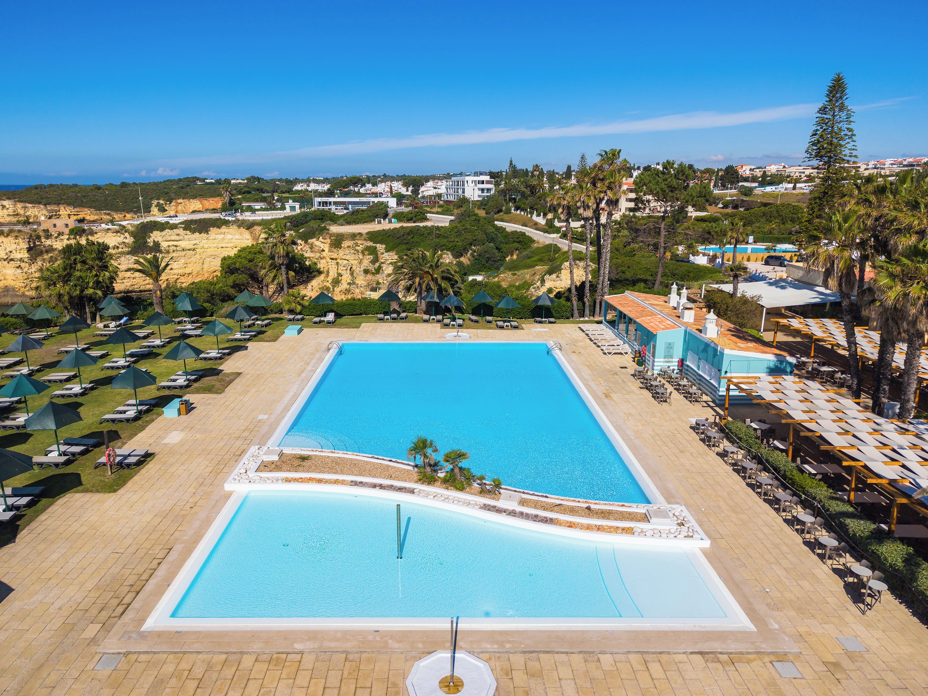 A large rectangular swimming pool with a tiled deck surrounding it, multiple lounge chairs, and umbrellas.