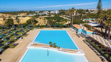 A large rectangular swimming pool with a tiled deck surrounding it, multiple lounge chairs, and umbrellas.