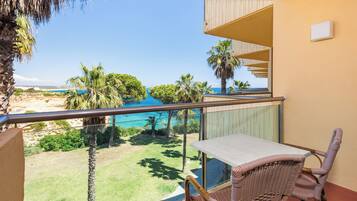 A balcony with a table and wicker chair, overlooking a beach and palm trees.