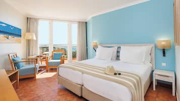 Habitación de hotel con cama, escritorio, silla y balcón con vistas.
