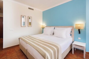 A neatly made bed with a striped blanket, two bedside lamps, and a small bedside table.