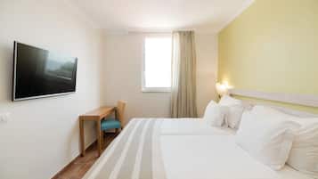 Habitación de hotel con cama, escritorio, silla, televisor montado en la pared y ventana con cortinas.