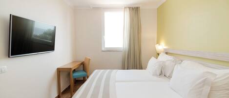 Ein Hotelzimmer mit Bett, Schreibtisch, Stuhl, Wandfernseher und einem Fenster mit Vorhängen.