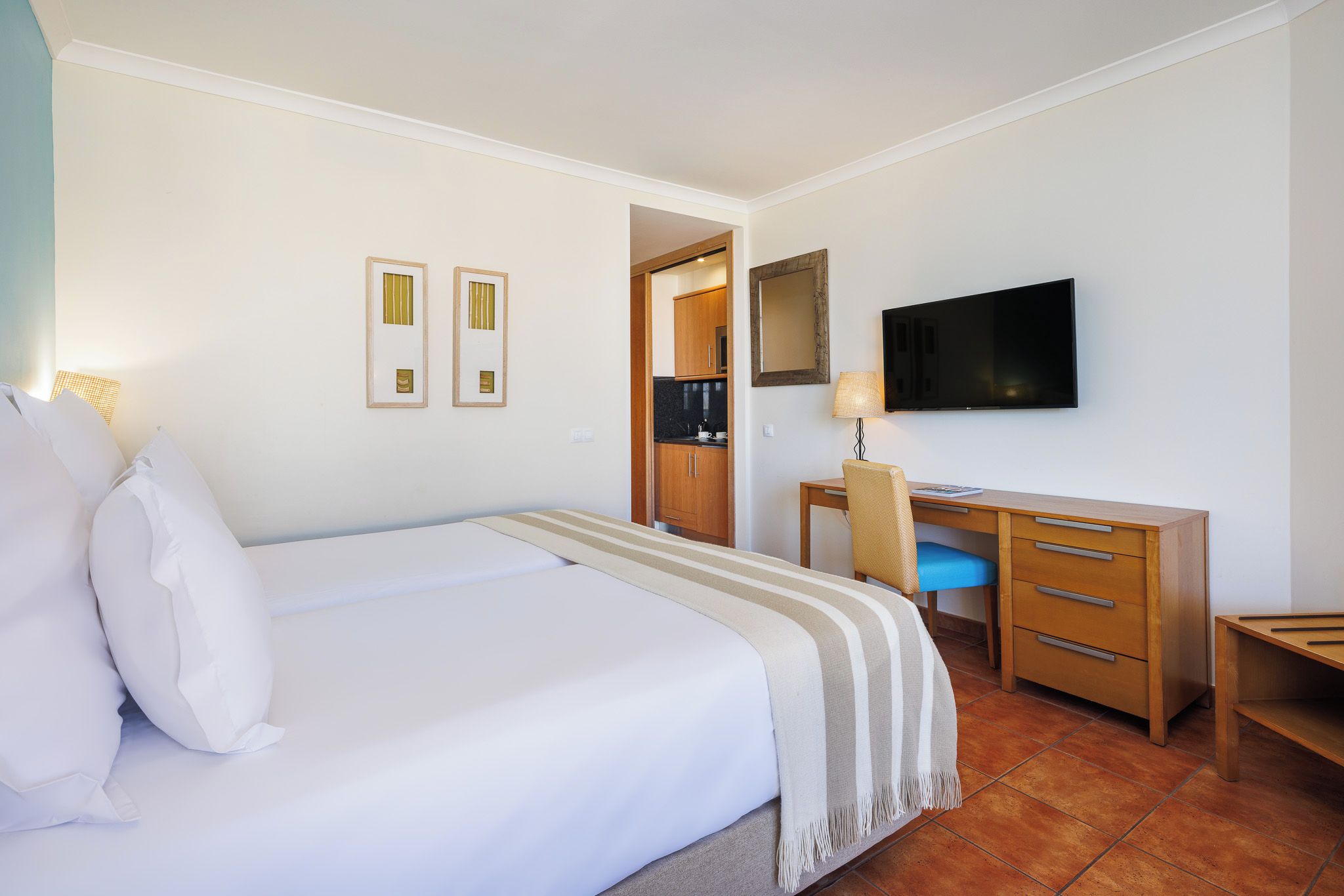A hotel room with a bed, a desk, a chair, a television, and a small kitchenette.