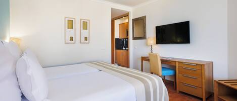 A hotel room with a bed, a desk, a chair, a television, and a small kitchenette.