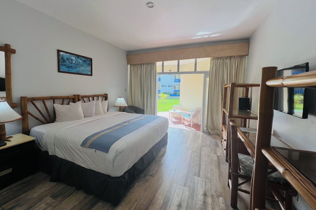 Ein Hotelzimmer mit Bett, Fernseher, Schreibtisch und Stuhl. Ein Fenster mit Vorhängen bietet einen Blick hinaus.