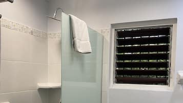 Un baño con cabina de ducha de vidrio, inodoro y ventana con persianas.