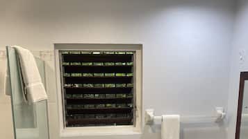 Un baño con cabina de ducha de vidrio, inodoro con ventana sobre él y lavabo con encimera de mármol.