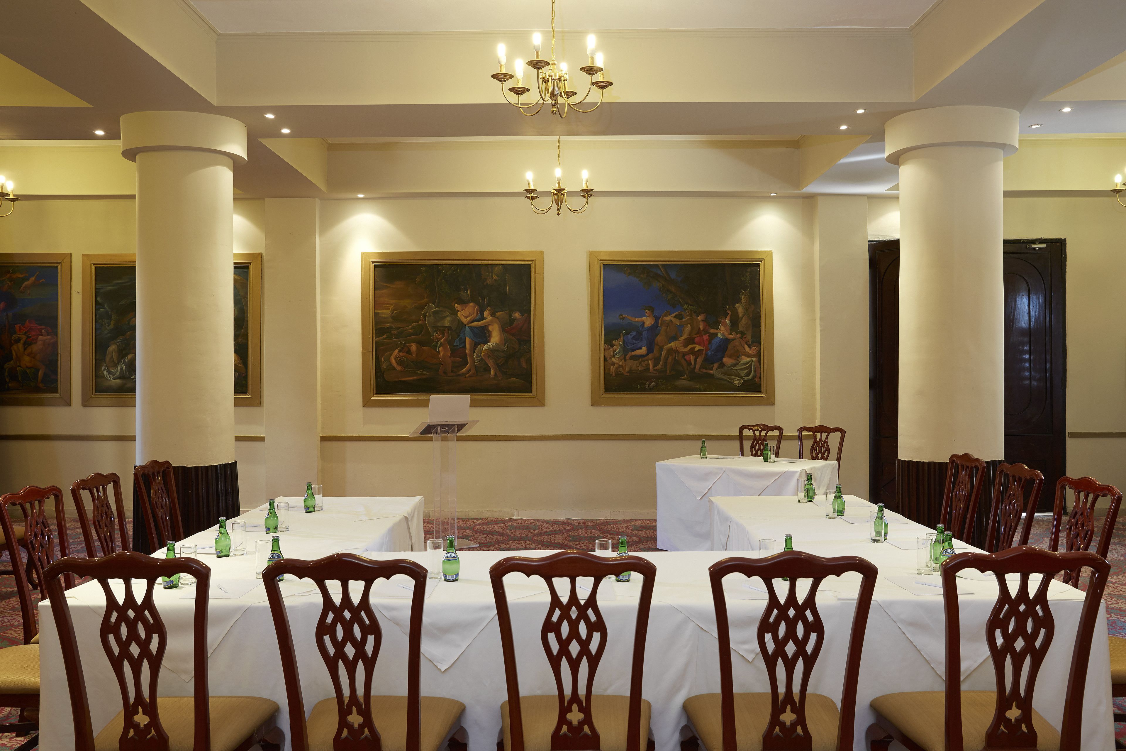 A formal dining room with a long table, chairs, and paintings on the walls.