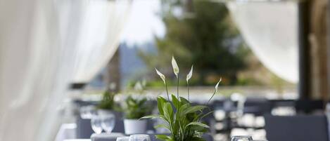A restaurant setting with tables set for dining, featuring potted plants and empty wine glasses.