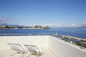 Un balcón con sillas blancas que da a una masa de agua, una isla rocosa y montañas distantes.