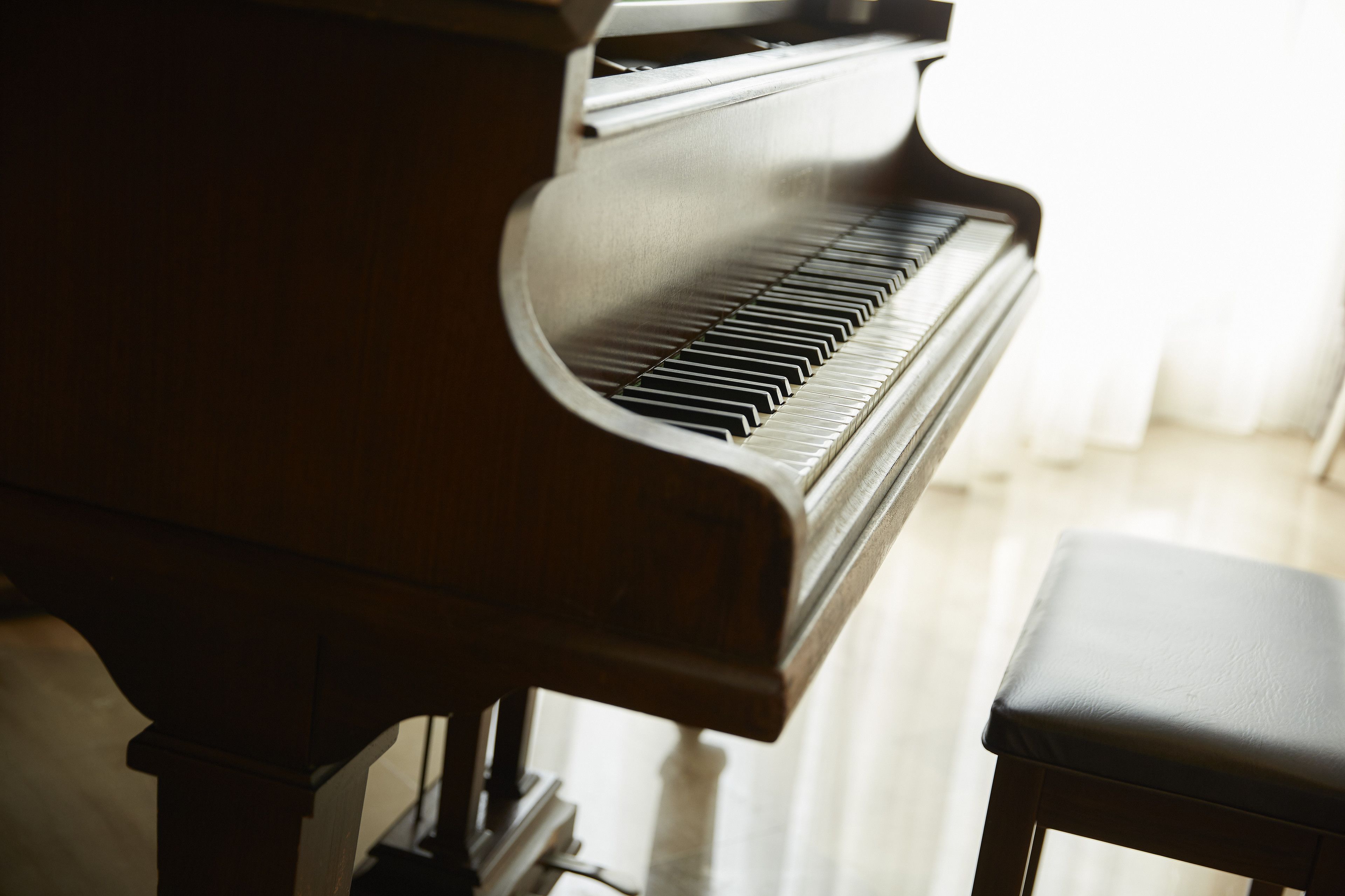 Un piano de cola con un banco en una habitación con piso de tonos claros y una ventana con cortinas.