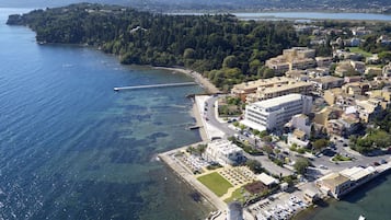 Vista aérea de uma cidade costeira com um porto, edifícios e uma ilha arborizada.