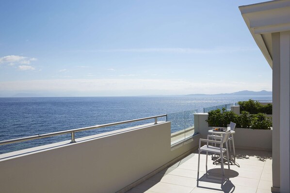 Un balcón con vista al mar, una mesa blanca con sillas y una barandilla.
