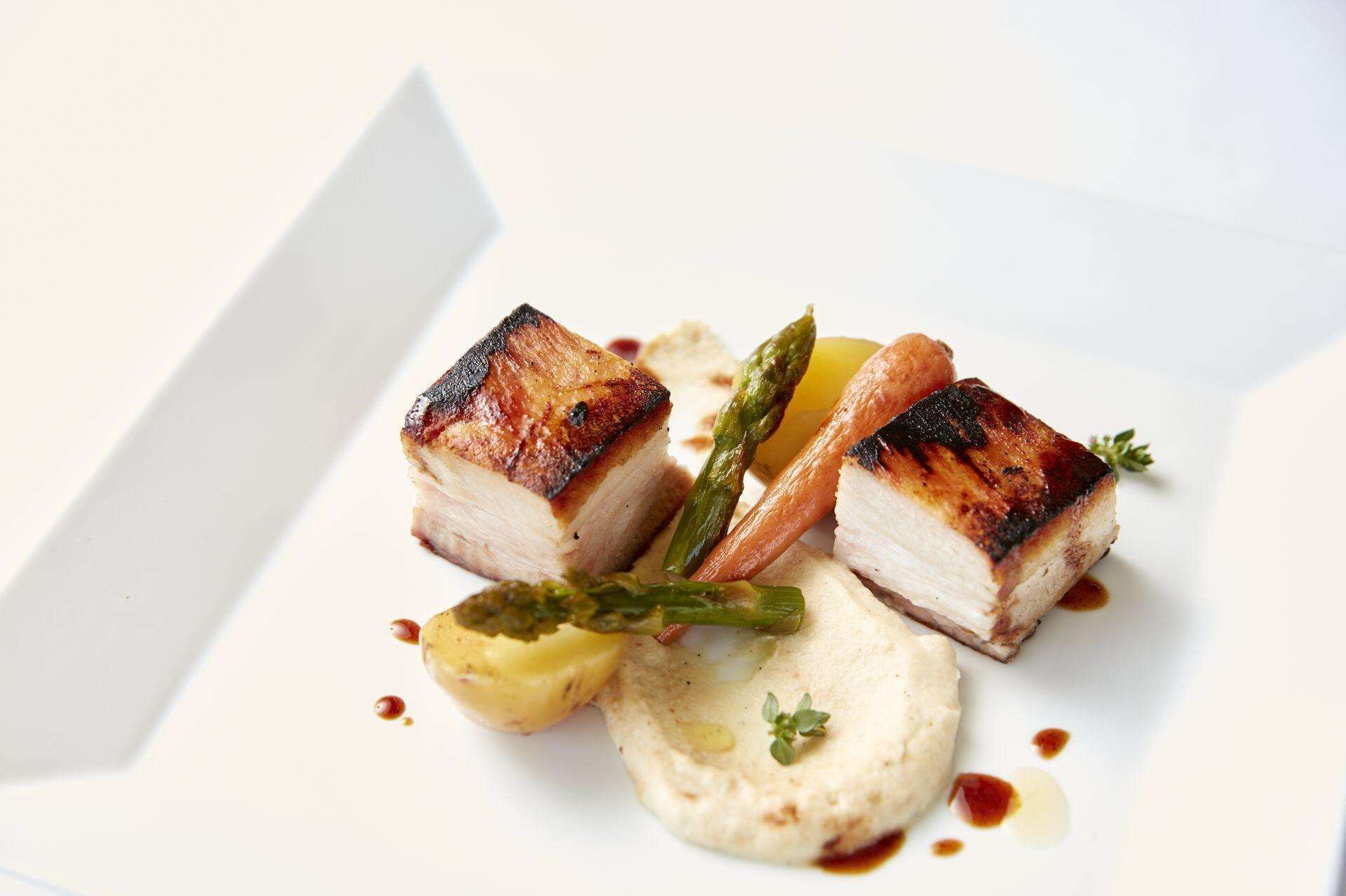 Un plat de viande grillée, accompagnée de légumes et de sauce, servi dans une assiette blanche.
