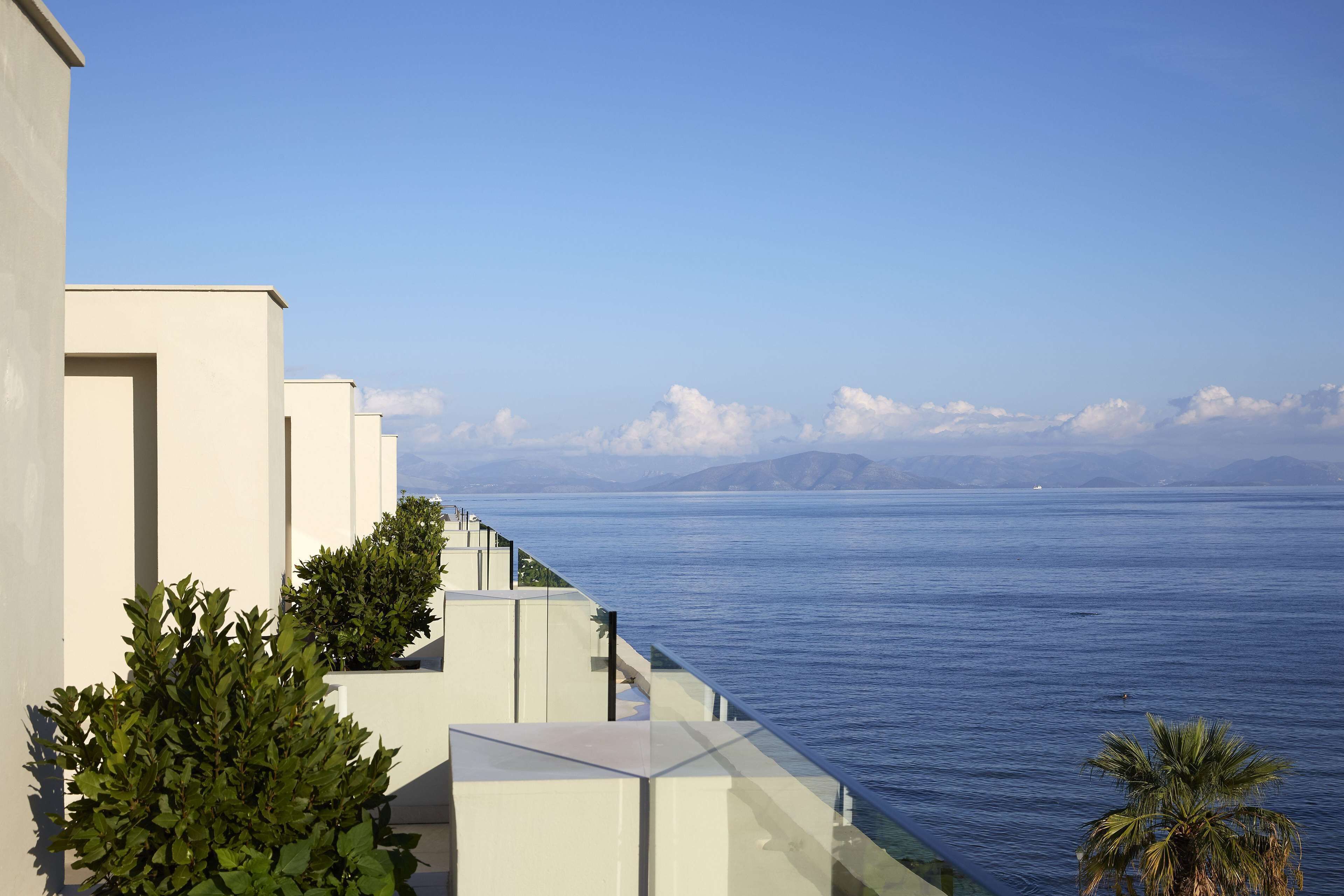 Een kusthotel met balkon, uitzicht op zee, heldere lucht en verre bergen.
