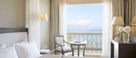 A hotel room with a bed, a chair, a small table, and a view of the sea through a balcony.
