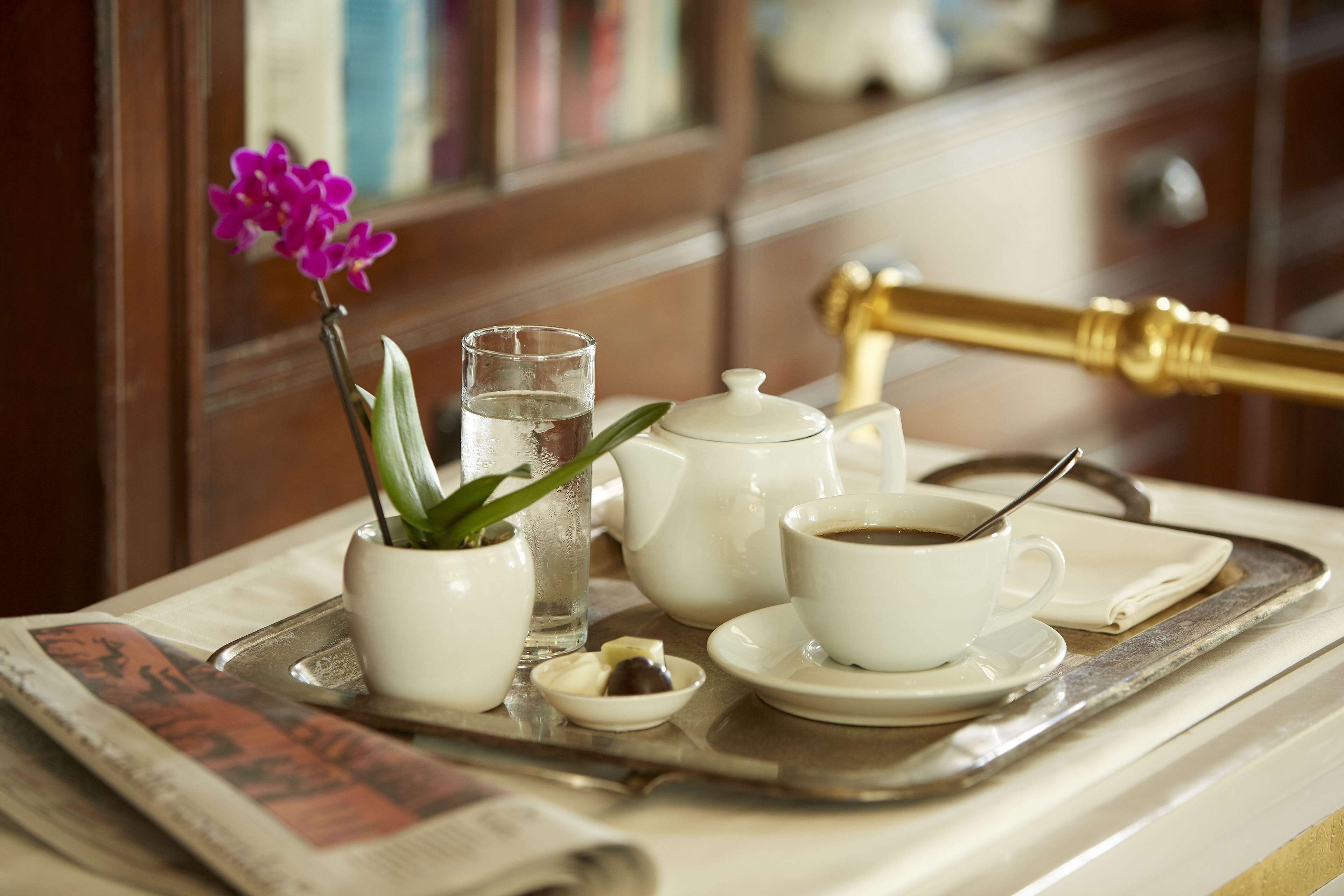 Un plateau avec une théière, des tasses, une cuillère, un petit bol de bonbons, un verre d’eau et une orchidée en pot.