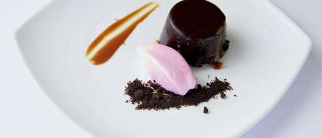 A dessert on a white plate with a caramel drizzle, a chocolate sphere, and a scoop of pink ice cream.
