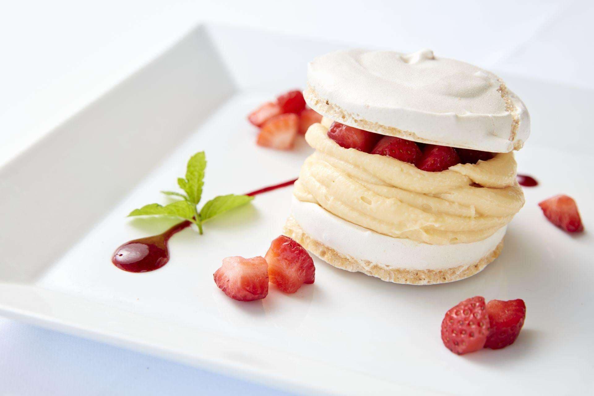 A dessert with layers of cream and strawberries on a white plate.