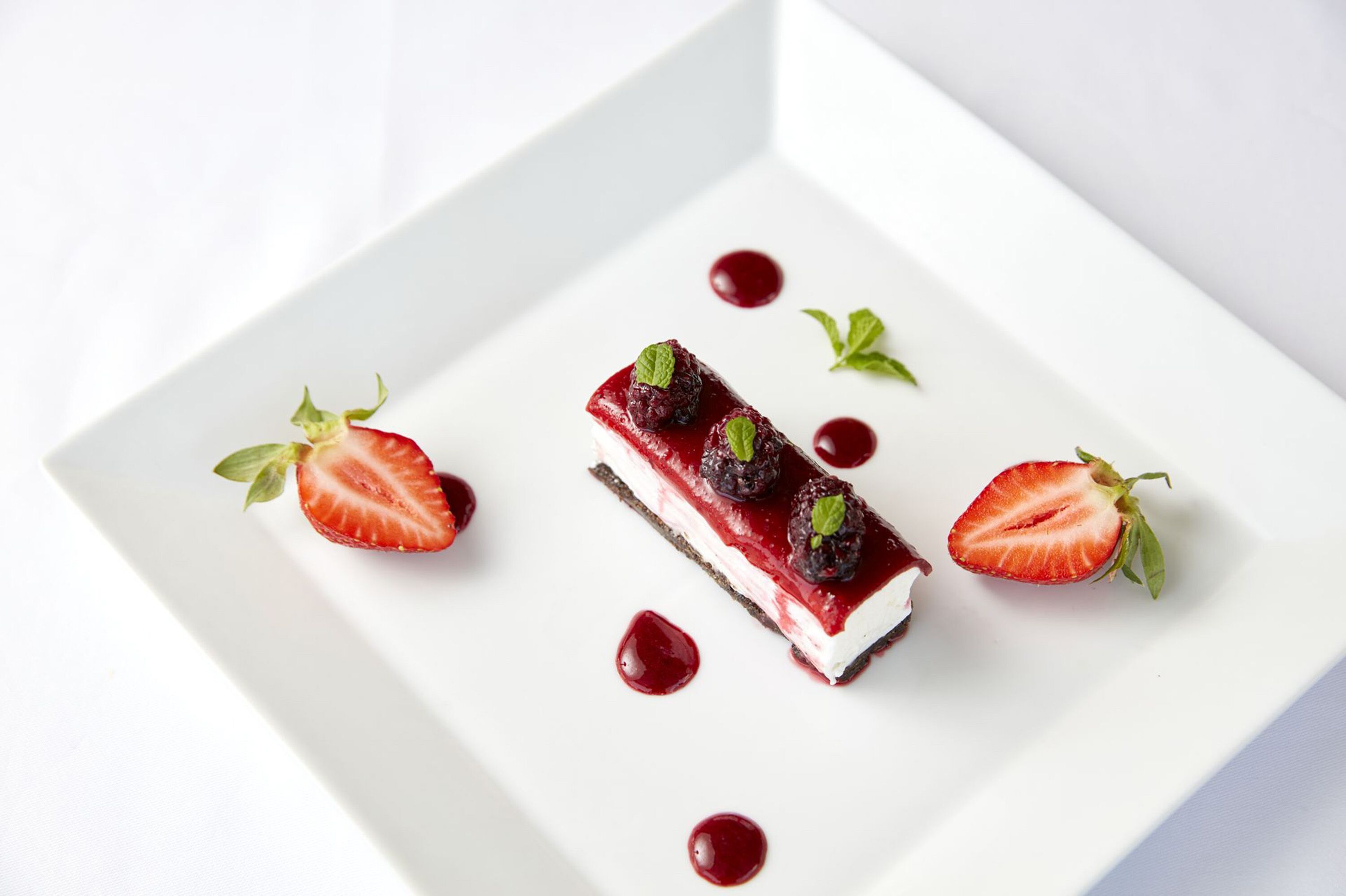 Un postre en un plato blanco con fresas y hojas de menta.