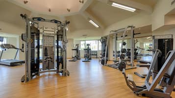 Un gimnasio espacioso con diversas máquinas de ejercicio, cinta de correr y pared de espejos.