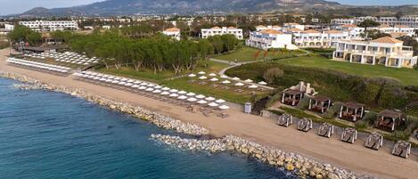 A coastal resort with a beach, multiple villas, and a view of mountains.