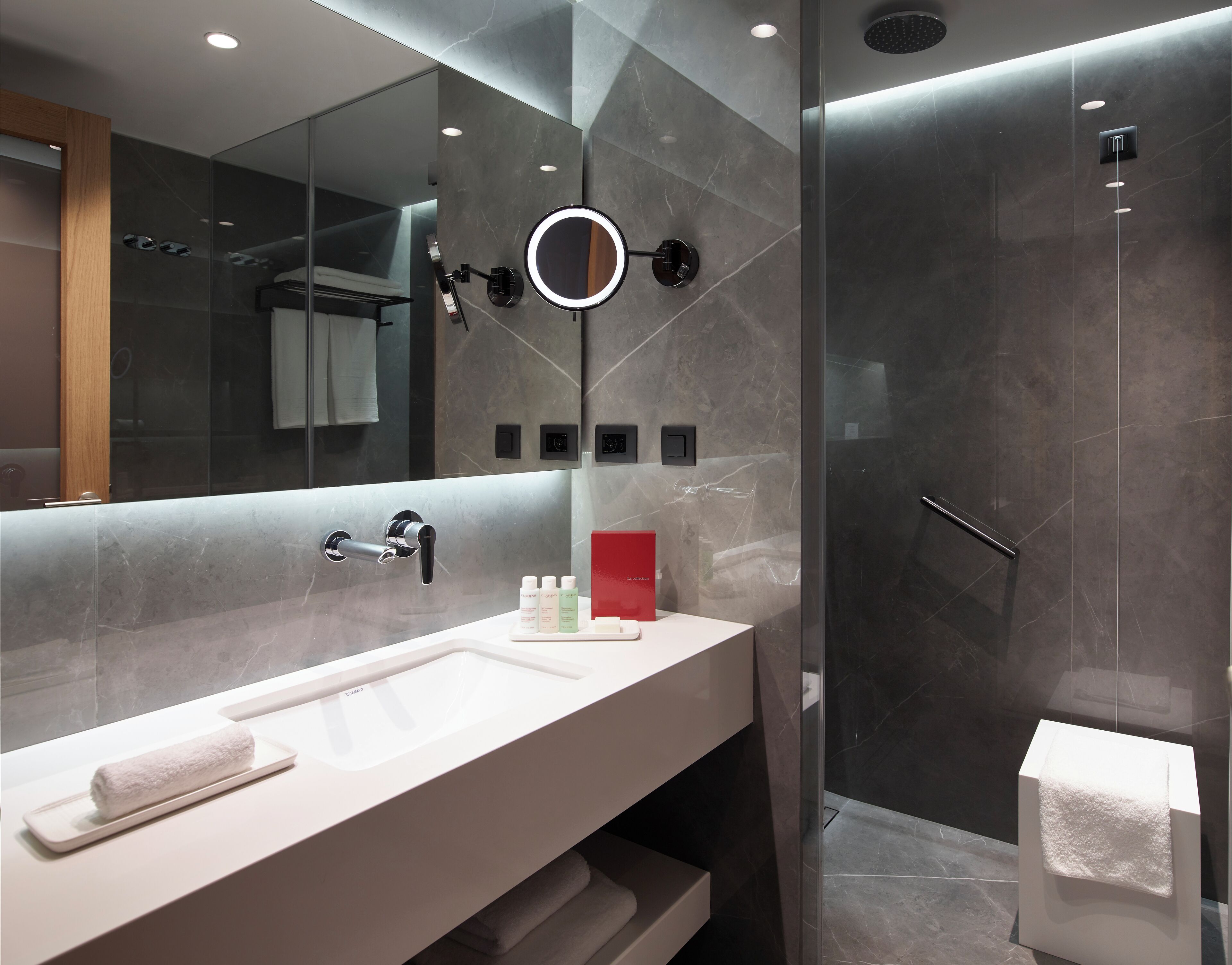 Un baño moderno con un espejo grande, un tocador con lavabo y una ducha con mampara de vidrio.