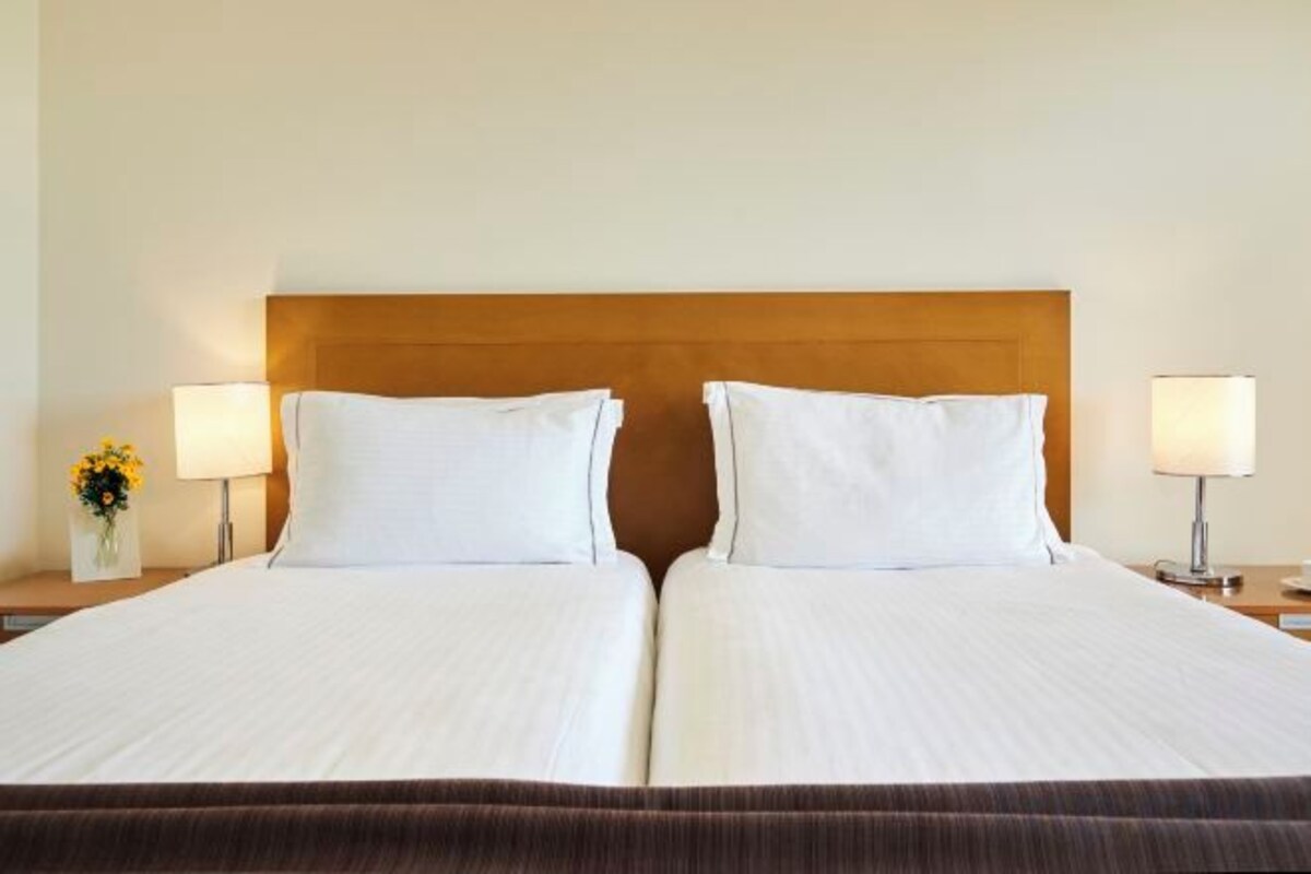 Una cama doble con sábanas blancas, dos lámparas de noche y un cabecero de madera.