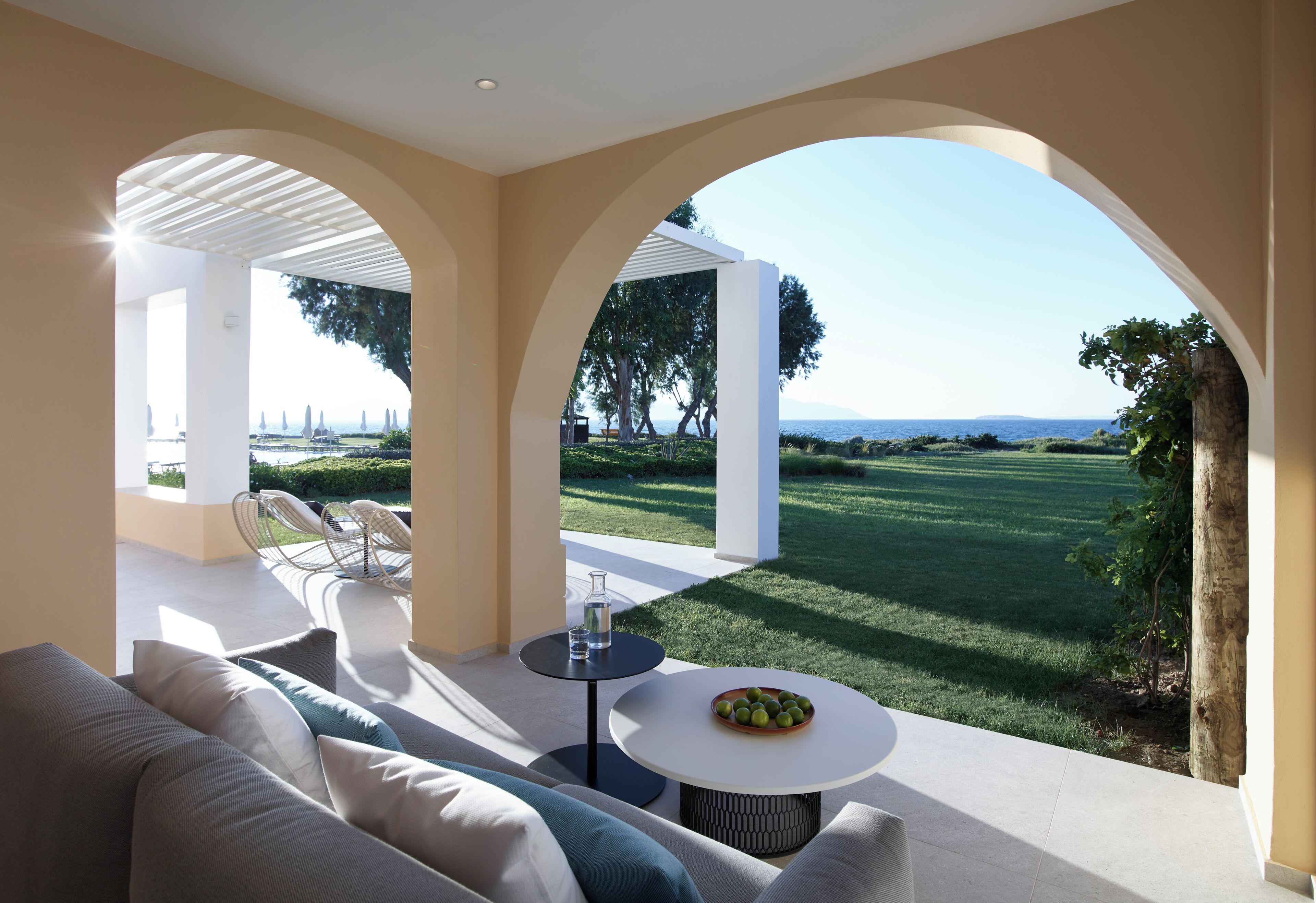 A modern outdoor seating area with a sofa, chairs, and a table, overlooking a well-maintained lawn and distant landscape.