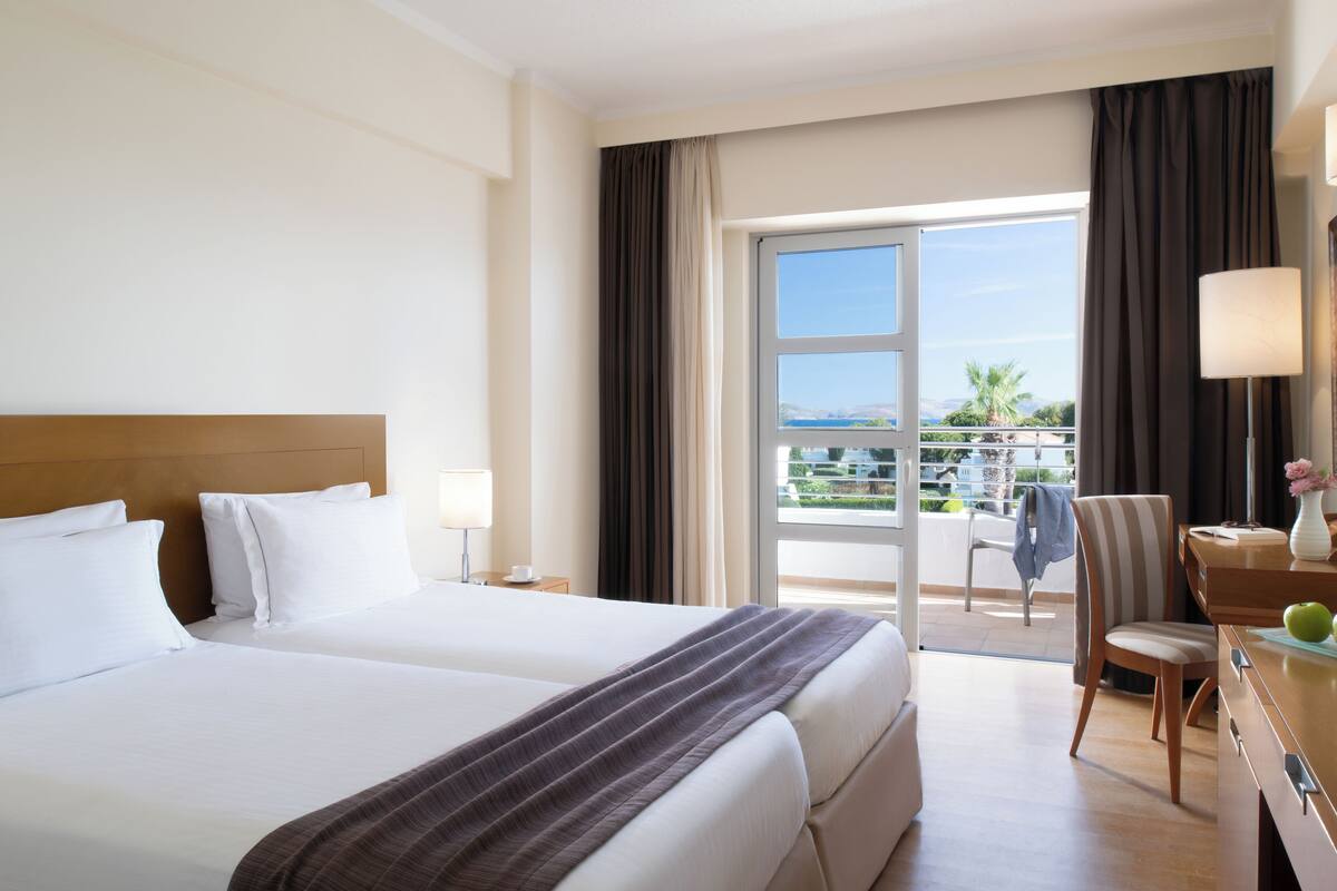 A hotel room with a large bed, a desk with a lamp, and a view of the outdoors.
