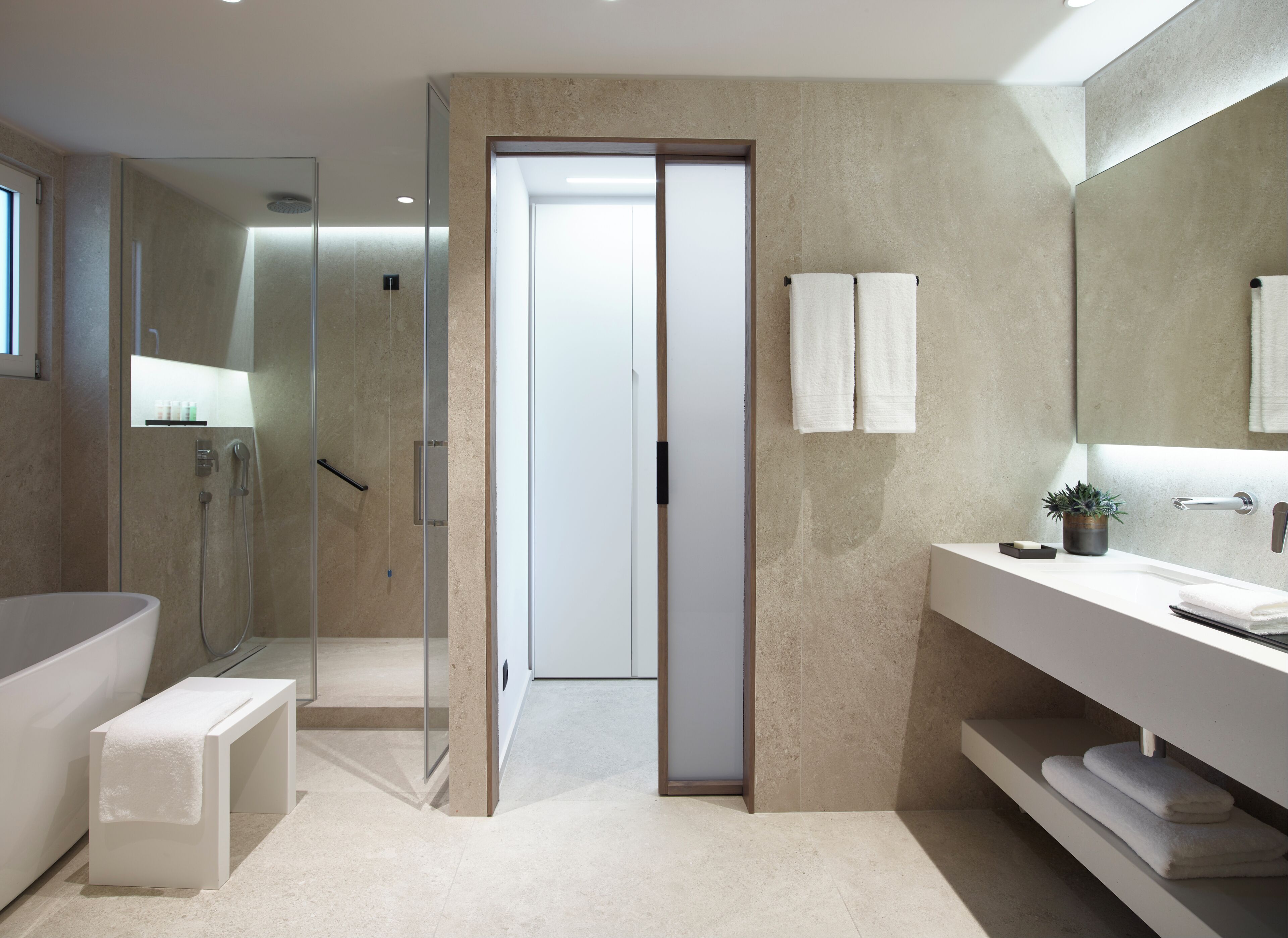 A modern bathroom with a glass-enclosed shower, a large bathtub, a vanity with a mirror, and a potted plant.