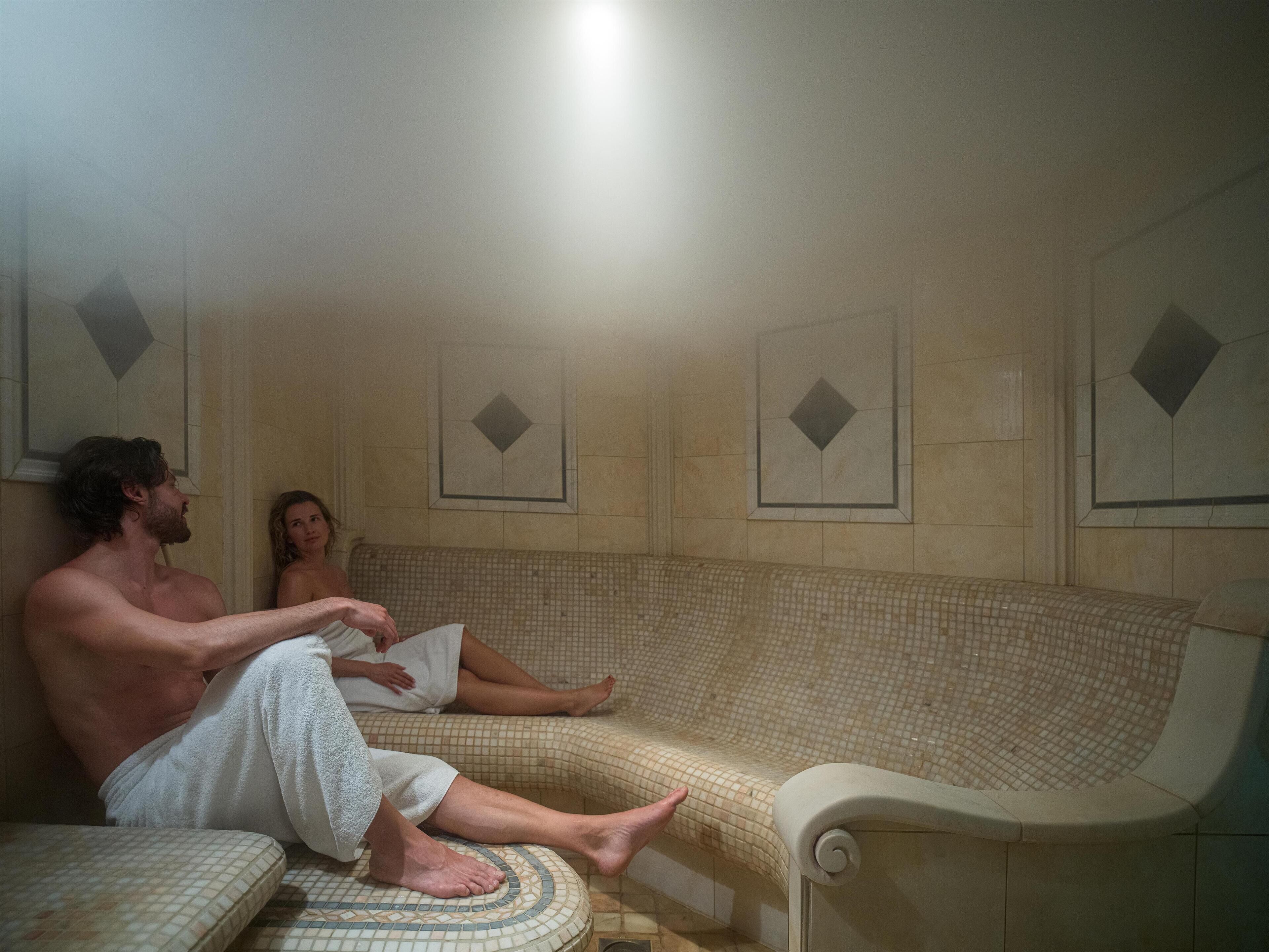 Una sauna con paredes y bancos de azulejos, suelo de cerámica y un calentador en la pared.