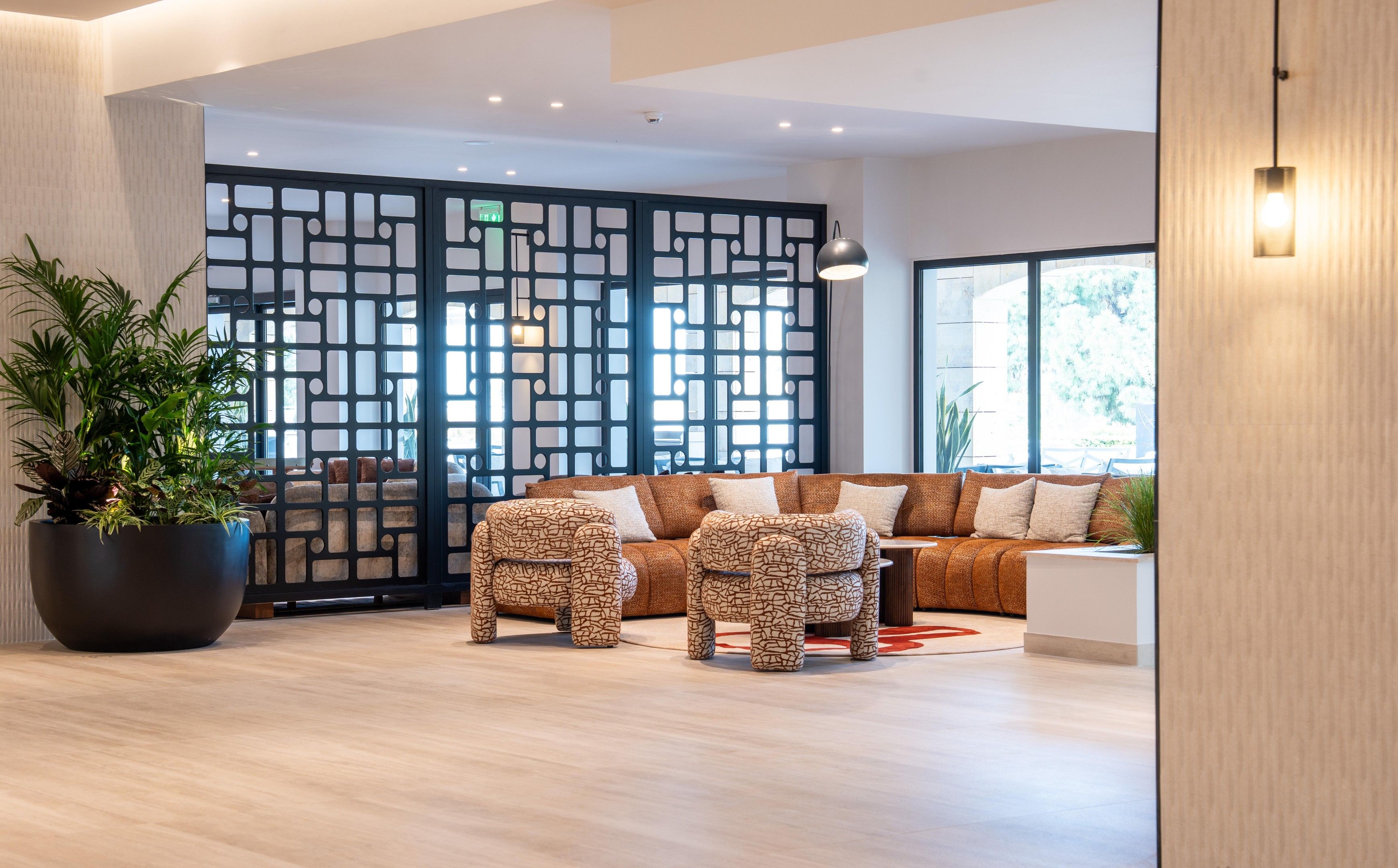 A modern living room with a sectional sofa, two matching ottomans, a large potted plant, and a decorative screen.
