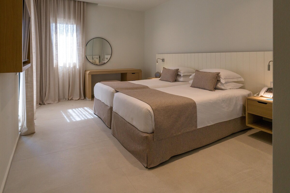 A hotel room with a large bed, bedside tables, a desk, and a mirror.