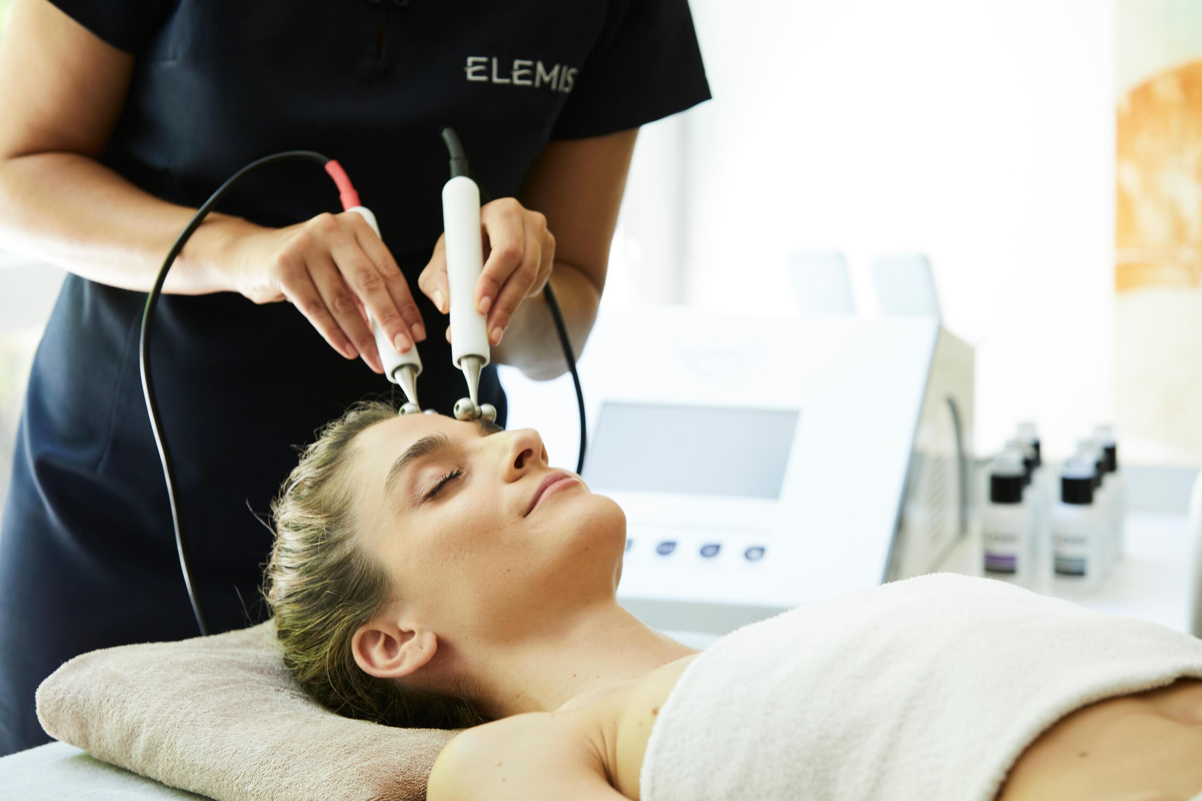 A person lying on a treatment bed receiving a facial treatment.