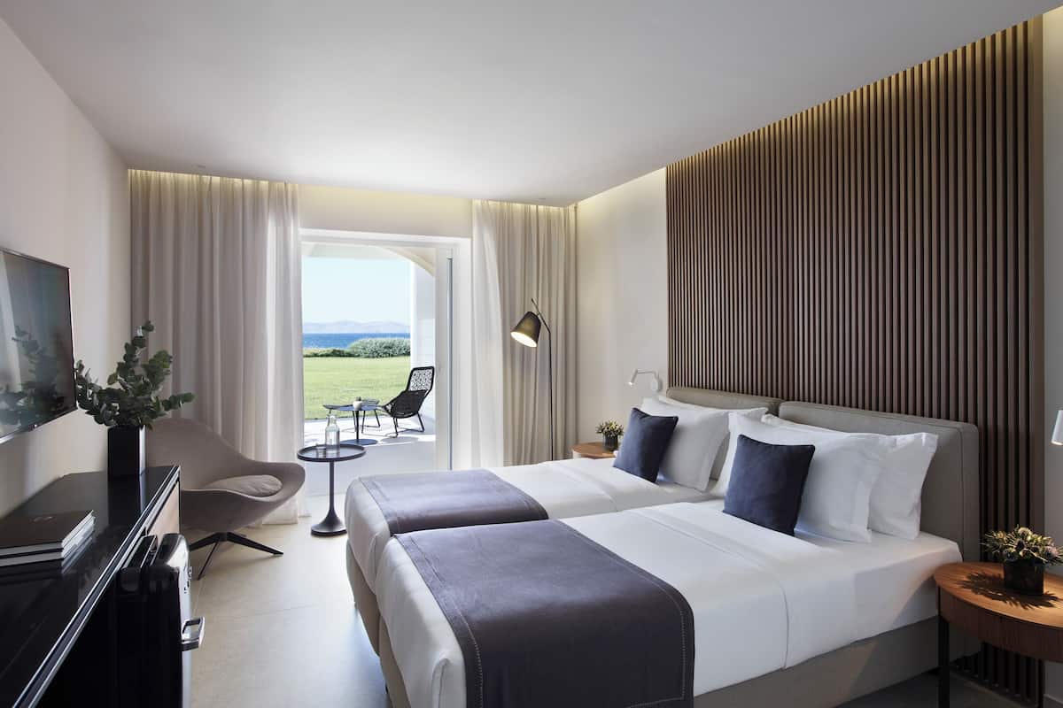 A hotel room with two beds, a TV, a desk, a chair, and a view of the outdoors.